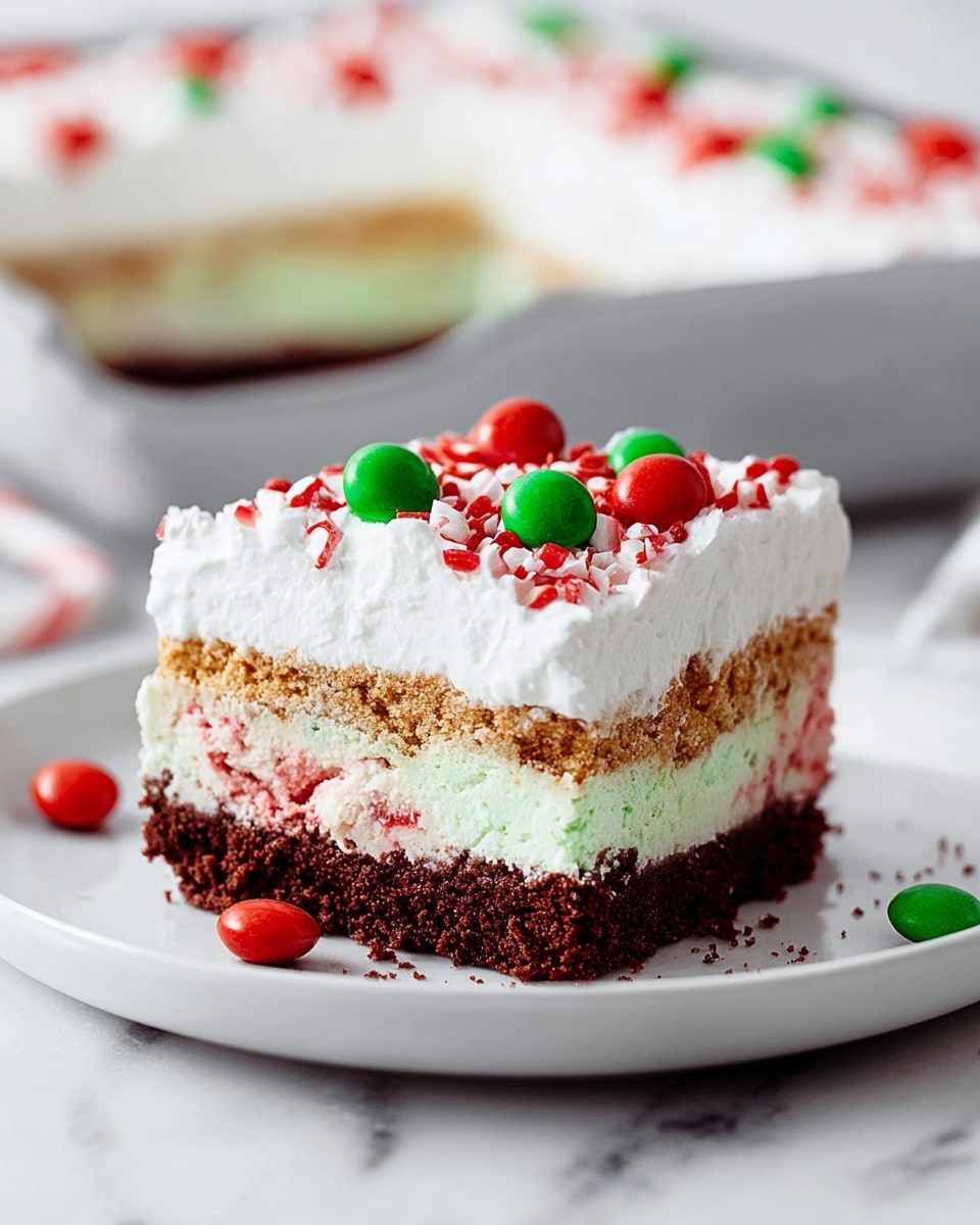 A square layered dessert sits on a white plate placed on a white marbled surface. The bottom layer is dark brown and crumbly, topped by a thick creamy white layer mixed with a hint of crushed red candy pieces. Above this is a golden cookie crumb layer, covered by a thick and fluffy white whipped cream topping. The top is decorated with small red and green round sprinkles scattered evenly and larger red candy pieces spread across the surface. Around the plate are red and green candy pieces and a chocolate sandwich cookie. The background is softly blurred with warm bokeh lights and hints of Christmas decoration. Photo taken with an iphone --ar 4:5 --v 7