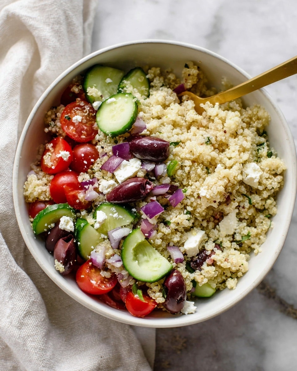 A white bowl filled with a colorful quinoa salad shows layers of small, fluffy, light beige quinoa grains as the base. On top, there are cut cucumber slices with deep green skin and a crisp texture, halved bright red grape tomatoes, chunky white feta cheese cubes, and small pieces of purple-red onion. Dark purple Kalamata olive halves are scattered around, adding contrast to the mix. A gold spoon rests inside the bowl, partially covered by the salad. The bowl sits on a white marbled surface with a soft white cloth nearby. photo taken with an iphone --ar 4:5 --v 7