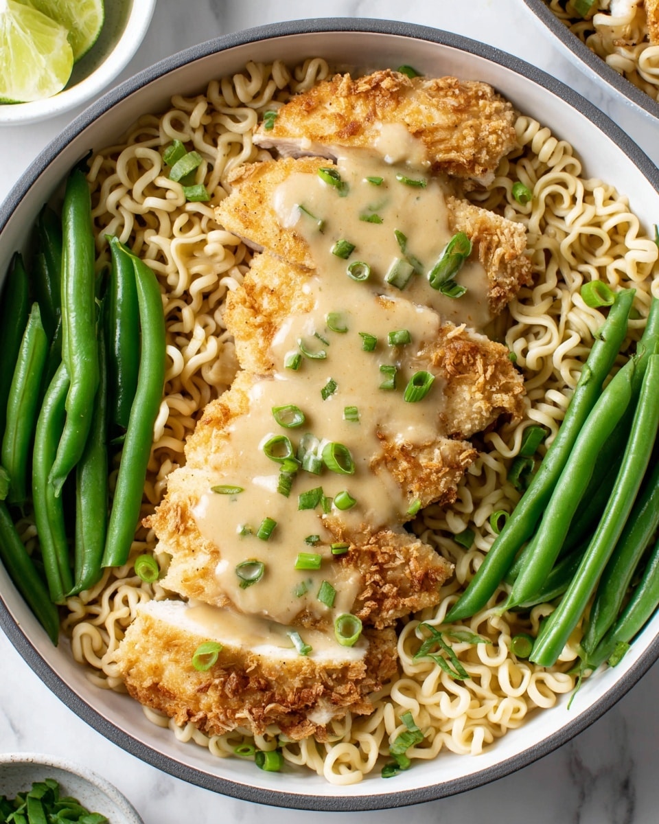 A white round bowl is filled with a layer of curly light beige noodles at the bottom, topped with five pieces of golden-brown fried chicken breasts, each covered with a creamy light beige sauce sprinkled with small chopped green onions. On the left and right edges of the bowl, there are several bright green, fresh green beans arranged in neat clusters. The background is a white marbled texture and there is a partial view of a white bowl with lime wedges at the top left corner. photo taken with an iphone --ar 4:5 --v 7