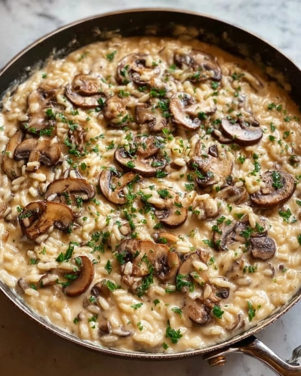 The image shows a skillet filled with creamy mushroom risotto. The dish has a smooth and creamy light beige sauce with cooked short-grain rice, topped with sliced brown mushrooms scattered evenly across the surface. Small bits of green herbs are sprinkled on top, adding a touch of color and freshness. The skillet is placed on a white marbled surface. Photo taken with an iphone --ar 4:5 --v 7