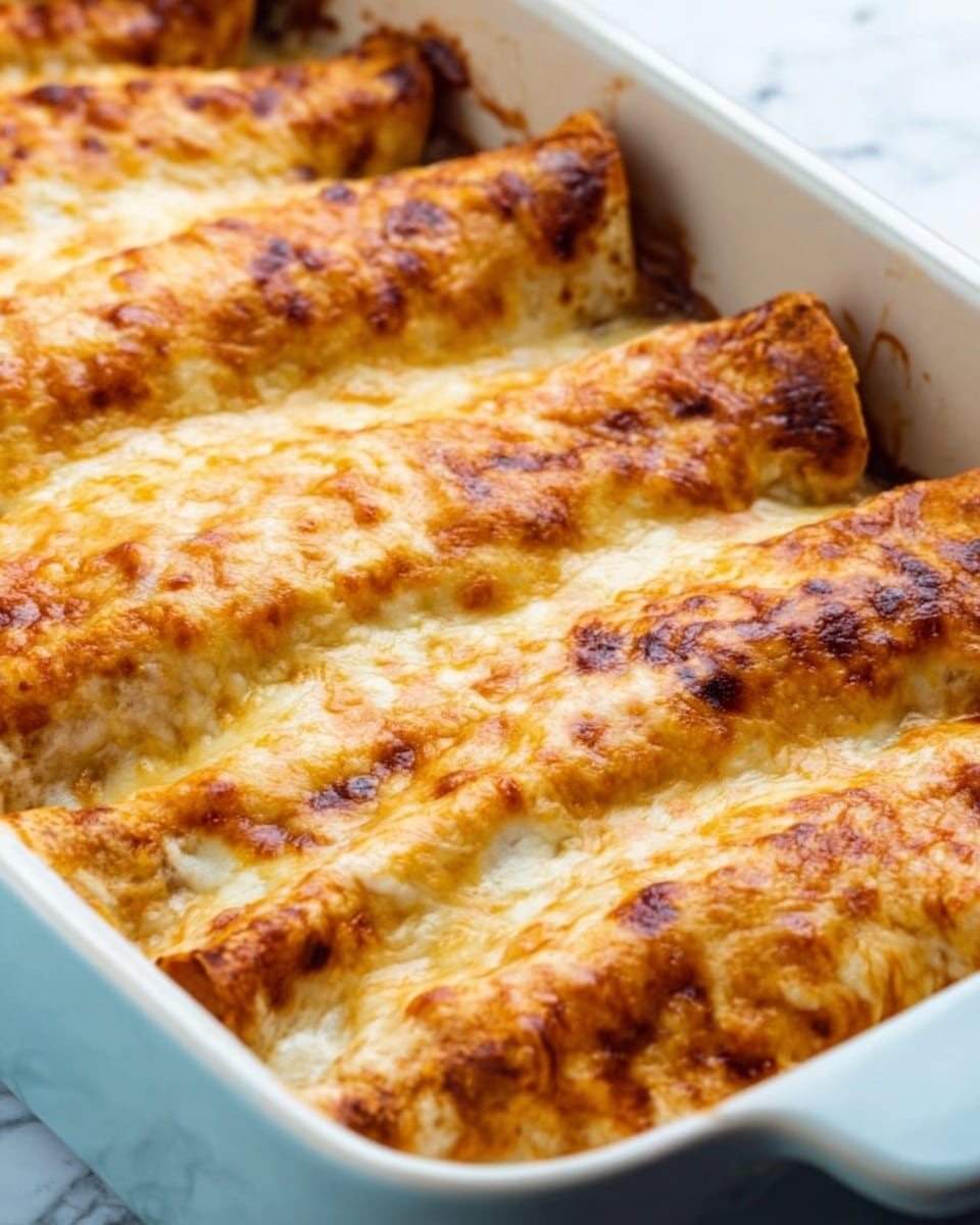 This image shows a white ceramic baking dish filled with five large rolled enchiladas placed side by side. Each enchilada has a golden-brown melted cheese layer on top, slightly bubbling and toasted unevenly to show light brown spots. The enchiladas themselves have a soft, off-white color underneath the cheese with a slightly crispy edge peeking out at the ends. The dish is placed on a white marbled surface that shines softly under light. Photo taken with an iphone --ar 4:5 --v 7