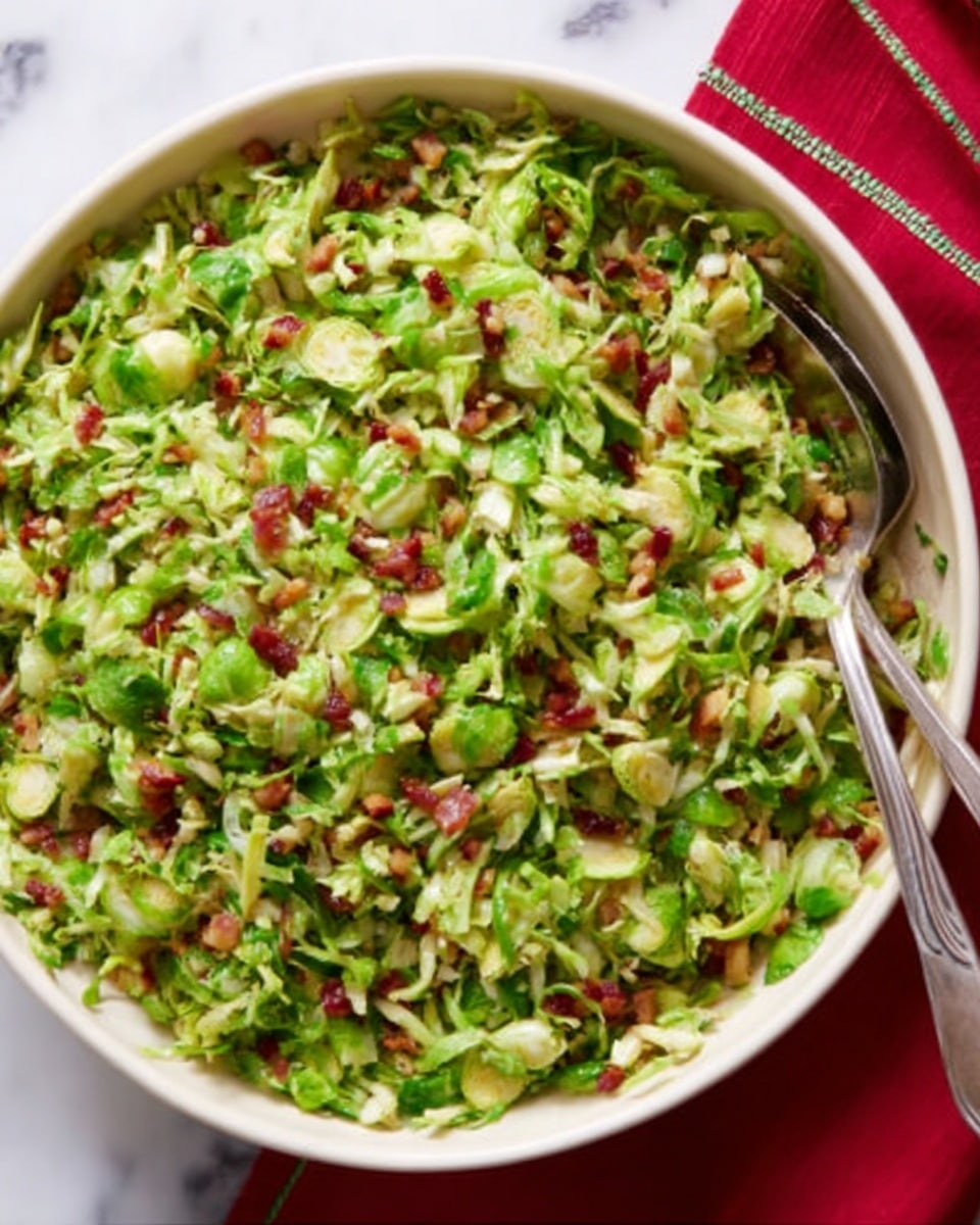 A round white bowl filled with finely shredded green Brussels sprouts mixed with small bits of red bacon or ham, lightly coated with a dressing that gives a slight shine. The Brussels sprouts have a crisp, thin texture and are layered evenly throughout the bowl, giving a fresh and vibrant look. A silver serving spoon and fork rest inside the bowl on opposite sides, and a folded red cloth with a thin white pattern is placed near the top right corner on a white marbled surface. photo taken with an iphone --ar 4:5 --v 7