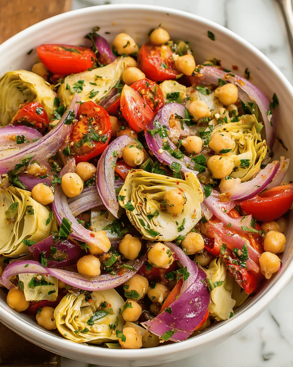 A close-up of a white bowl filled with a colorful salad featuring one main layer of round beige chickpeas scattered throughout, mixed with bright red halved cherry tomatoes, and topped with pale yellow artichoke hearts cut into halves and quarters, layered on top with thin slices of purple-red onion rings and chopped green herbs evenly spread over the salad. The bowl is set on a white marbled texture surface. Photo taken with an iphone --ar 4:5 --v 7