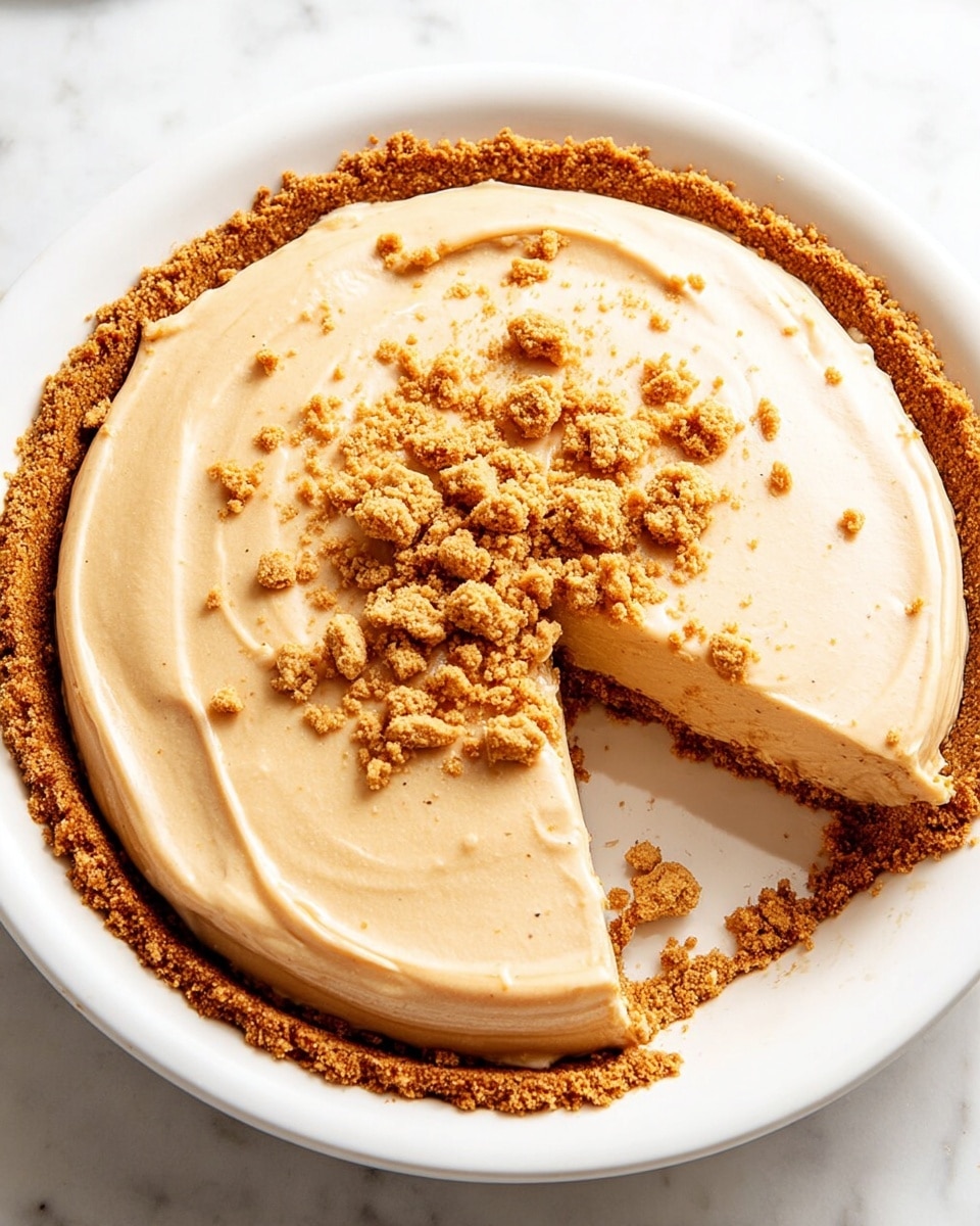 A round pie with three visible layers sits on a white pie dish placed on a white marbled surface. The bottom layer is a thick crumbly crust of golden brown color that lines the dish's edge. The middle layer is a smooth, creamy filling in a light beige tone that is evenly spread above the crust. On top, scattered in the center, are medium-sized clusters of crumbly golden brown crumbs matching the crust. The texture contrasts between the rough crust, silky cream, and crunchy crumbs create an inviting look. Photo taken with an iphone --ar 4:5 --v 7