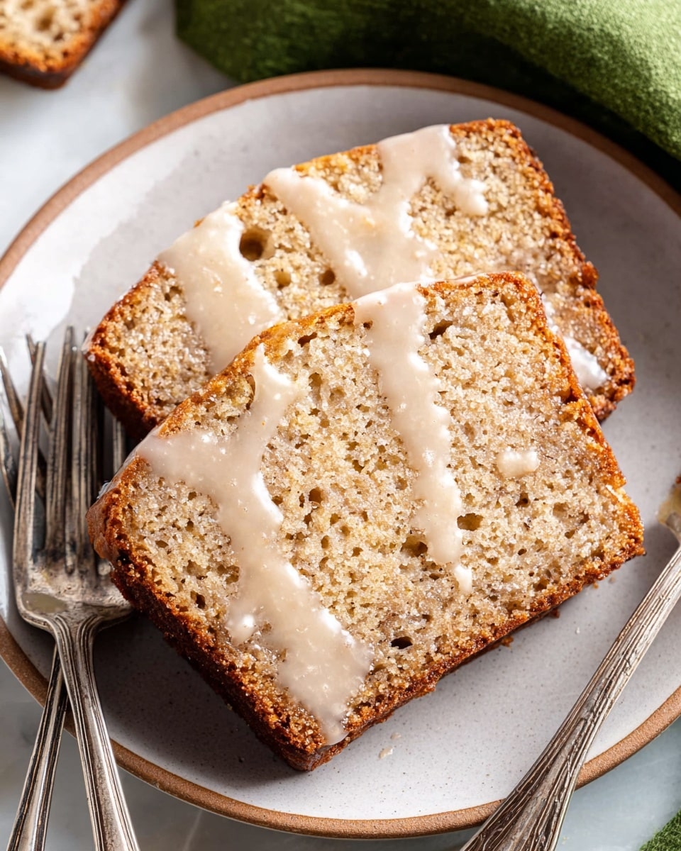 Two thick slices of light brown, moist cake with a slightly rough and porous texture are placed side by side on a white plate. A thin, glossy layer of light beige glaze is drizzled unevenly over the top slice, pooling slightly at the edges and dripping down. The plate sits on a white marbled surface, and two old-fashioned silver forks are resting beside the slices. Photo taken with an iphone --ar 4:5 --v 7