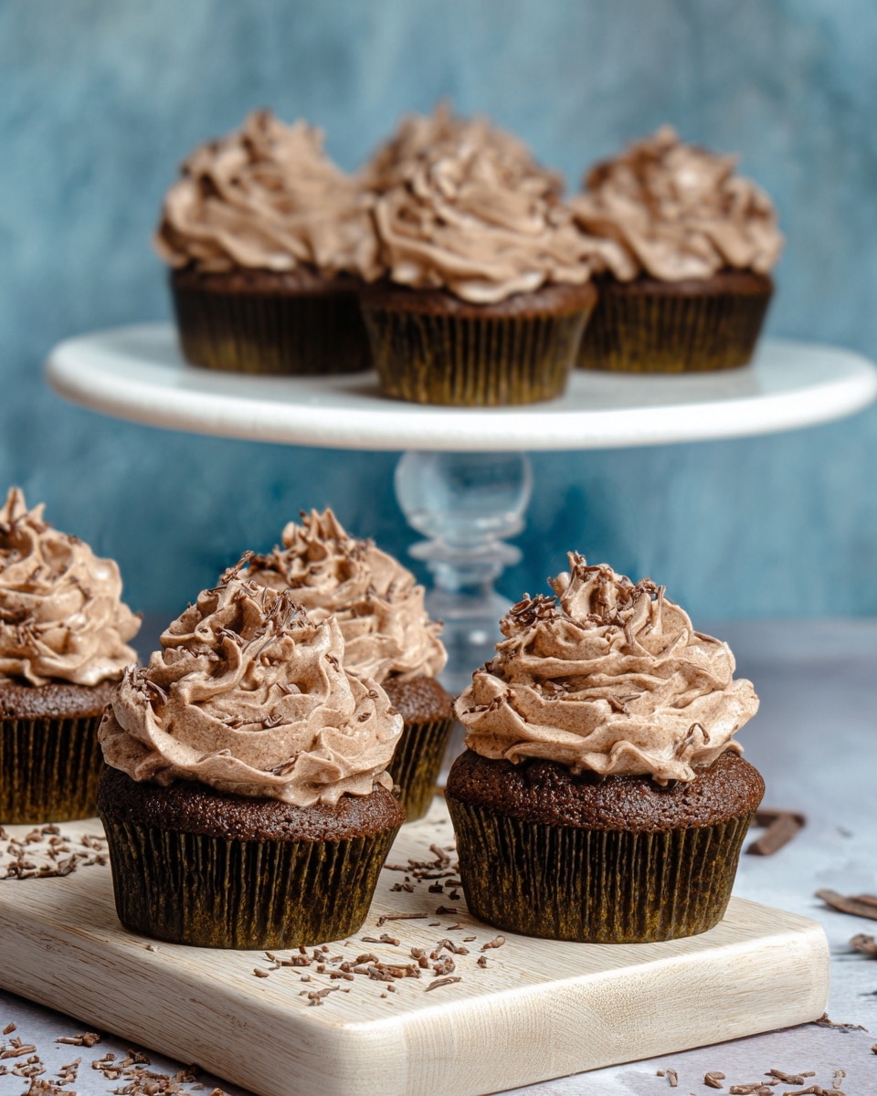 A group of six chocolate cupcakes with dark brown cake bases and rich swirled chocolate frosting on top, three cupcakes are lined up on a wooden board with chocolate shavings around them, and the other three are placed on a white plate with a golden rim elevated by a clear stand, all set against a white marbled texture, the frosting has a smooth, creamy texture with decorative swirls that rise in soft peaks. photo taken with an iphone --ar 4:5 --v 7