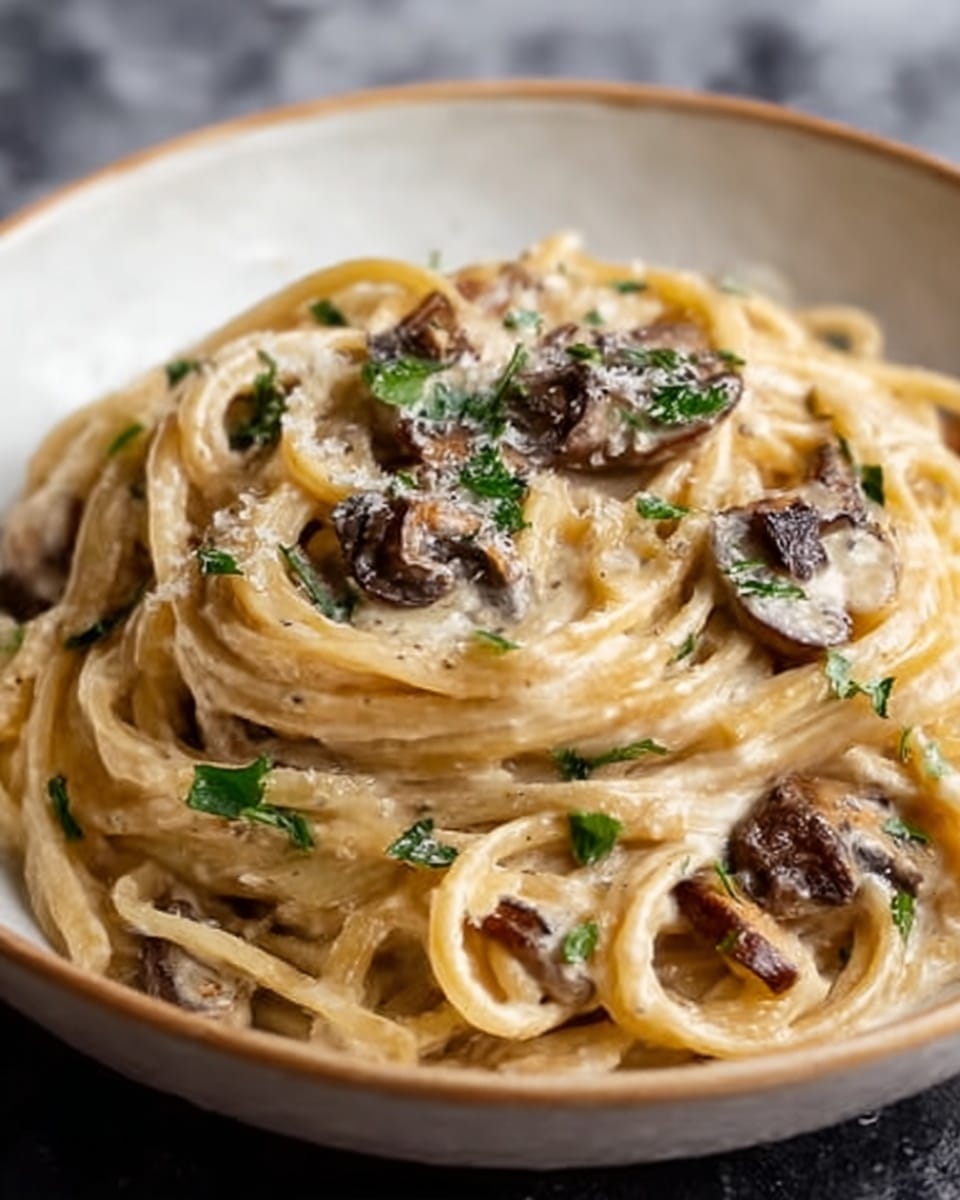A close-up of creamy fettuccine pasta served in a white bowl, showing three layers: the bottom layer is smooth and shiny fettuccine noodles in a pale yellow color, the middle layer has small pieces of cooked mushrooms scattered evenly, and the top layer is garnished with fresh green herbs and a light sprinkle of grated cheese, adding texture and a contrast of color. The creamy sauce is visible clinging to the noodles with a slightly glossy look. The surface beneath the bowl is white with a marbled texture. Photo taken with an iphone --ar 4:5 --v 7