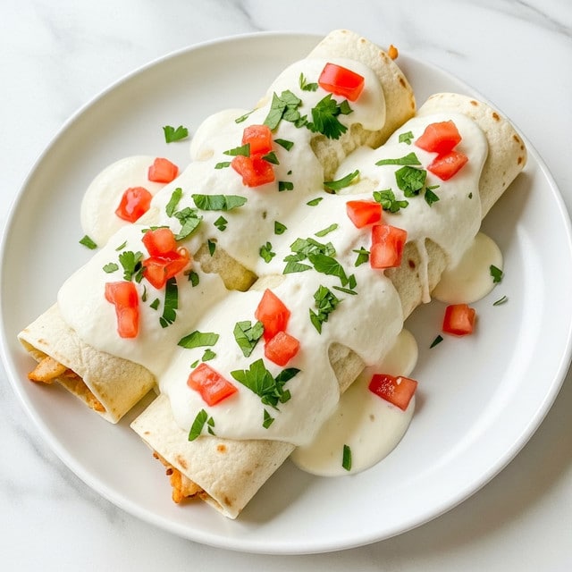 A white plate holds three rolled enchiladas covered with melted white cheese and light brown sauce. On top of the cheese layer, there are small bright red tomato pieces and finely chopped green herbs scattered across the dish, adding fresh color. The edges of the enchiladas are slightly crispy and golden, showing a warm, baked texture underneath. The plate sits on a white marbled surface. photo taken with an iphone --ar 4:5 --v 7