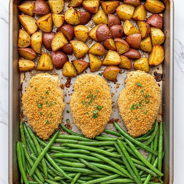 This image shows a baking tray filled with roasted food placed on a white marbled texture. At the top are golden brown roasted potato pieces with some red skin, scattered unevenly. In the middle, there are three evenly spaced breaded chicken breasts with a crunchy, golden crust sprinkled with small green herbs. At the bottom, fresh green beans are gathered in a thick layer, their shiny texture showing a light coating of oil. The overall look is warm and inviting with a mix of textures from crispy to tender. photo taken with an iphone --ar 4:5 --v 7