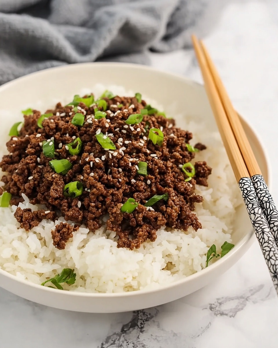 A white bowl filled with a bed of fluffy white rice forming the bottom layer, topped with a generous serving of cooked ground beef that is dark brown and slightly crumbly in texture. The beef is garnished with small green onion slices scattered evenly and sprinkled with white sesame seeds. Resting on the edge of the bowl are light brown wooden chopsticks with decorative black and white tips. The bowl is placed on a white marbled surface with a gray cloth blurred softly in the background. photo taken with an iphone --ar 4:5 --v 7