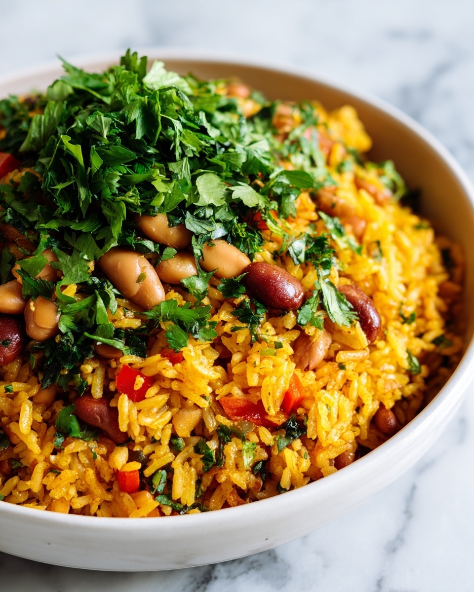 A close-up view of a white bowl filled with a colorful rice dish showing roughly three main layers: the base is fluffy orange-tinted rice mixed evenly with small pieces of red and yellow diced vegetables; scattered on top are light brown beans adding a smooth texture; fresh green leafy herbs are chopped and sprinkled throughout, giving a bright, fresh contrast. The rice looks moist and well cooked with a slight shine, and the vegetables appear soft but slightly firm. The setting is on a white marbled surface. photo taken with an iphone --ar 4:5 --v 7
