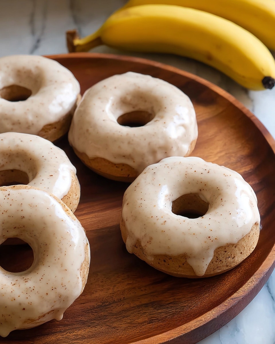 Five round donuts with a smooth, light beige glaze speckled with tiny brown dots cover each donut evenly. They are arranged close together on a round wooden board, showing the soft, slightly bumpy texture of the donuts beneath the shiny glaze. In the back, slightly out of focus, there are two yellow bananas resting on the wooden surface. The whole scene sits on a white marbled texture. photo taken with an iphone --ar 4:5 --v 7