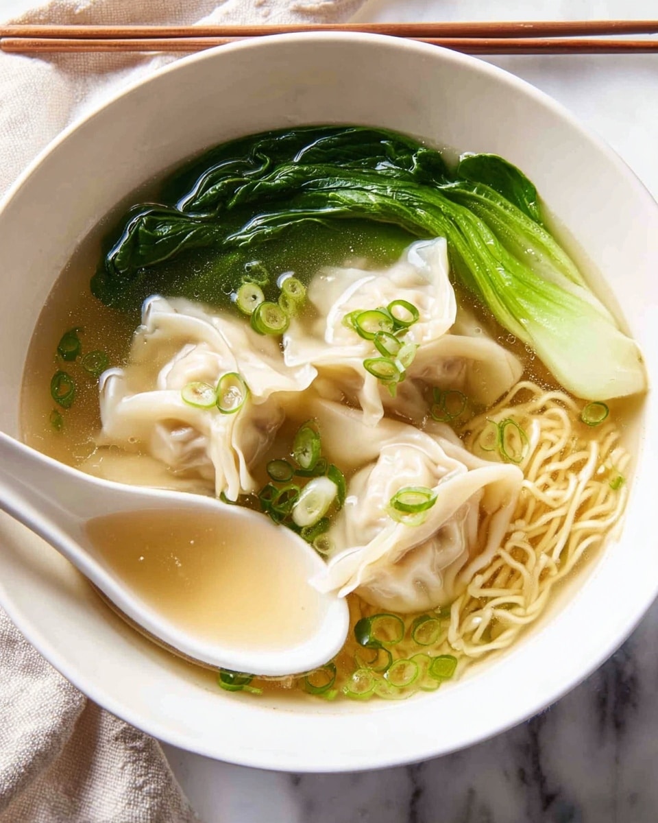 A bowl of clear broth noodle soup with three light-colored wontons floating near the center, the wontons showing soft, folded dough with some minced filling visible inside. A cluster of bright green leafy vegetables rests on the left side, partially submerged. Thin, pale yellow noodles curl at the bottom of the bowl. Small rounds and slices of fresh green onions are scattered on top, adding pops of green. A white ceramic spoon holds one wonton above the broth near the top of the bowl. The bowl sits on a white marbled surface with wooden chopsticks resting diagonally in the background. Photo taken with an iphone --ar 4:5 --v 7