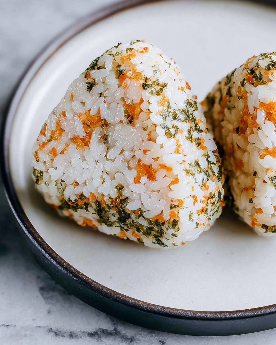 A close-up of a triangular rice ball showing layers of white sticky rice mixed with small orange bits and green specks, giving a textured look with a slight shine on the surface. It is placed on a white plate with a dark brown rim, all set on a white marbled texture. The rice grains are clearly visible, tightly packed, and the orange and green bits are evenly spread throughout the rice ball, adding color and texture contrast. Photo taken with an iphone --ar 4:5 --v 7