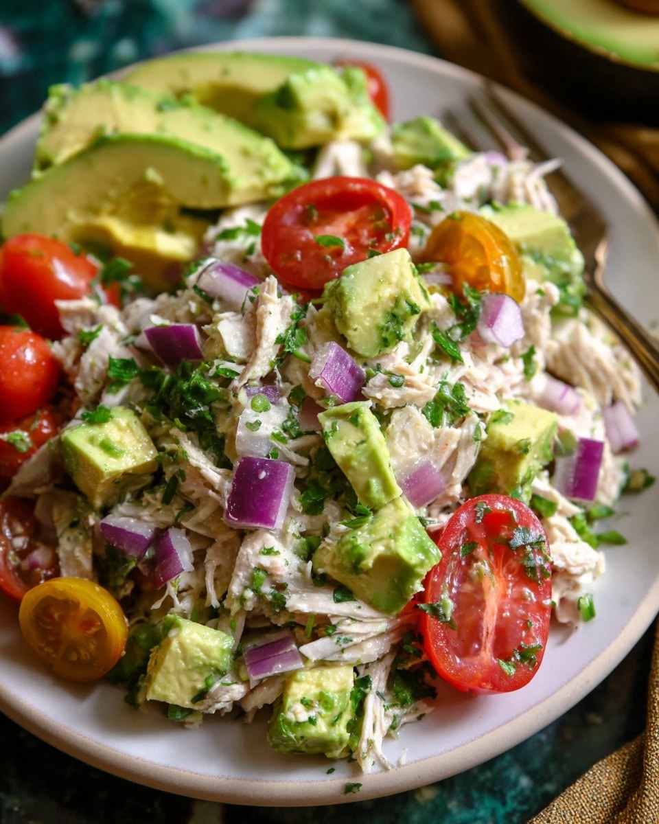 The image shows a white plate filled with a colorful chicken salad. The bottom layer has shredded white chicken mixed with finely chopped fresh green herbs. On top, there are chunks of bright green avocado and halved red cherry tomatoes. Small pieces of purple onion are spread throughout, adding contrast. The salad looks fresh and juicy with a mix of soft and firm textures, all placed on a white marbled surface. Photo taken with an iphone --ar 4:5 --v 7