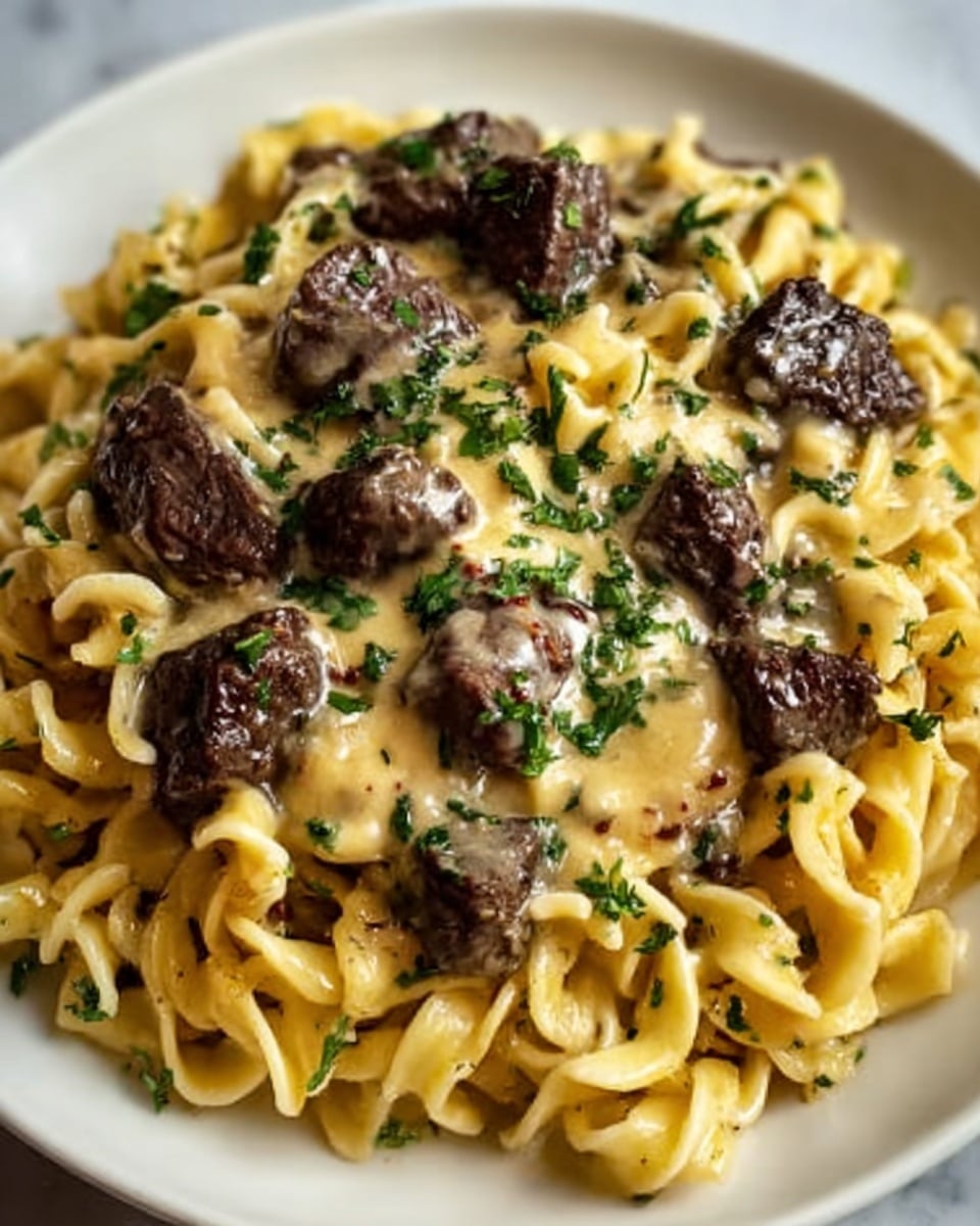 A close-up view of a creamy pasta dish on a white plate, featuring thick, twisted noodles coated in a smooth, light yellow cheese sauce. Generous chunks of dark brown beef are scattered over the pasta, mixed with small flecks of green herbs and fresh parsley sprinkled on top. The cheese sauce looks rich and slightly glossy, covering the pasta and meat evenly. The dish is placed on a white marbled surface with natural light highlighting the textures and colors. Photo taken with an iphone --ar 4:5 --v 7