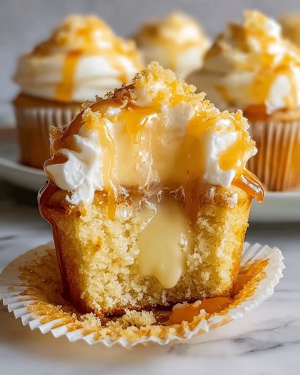 A close-up image of a cupcake with three visible layers: the bottom layer is a light golden yellow cake that looks soft and moist, the middle layer is creamy and pale yellow filling oozing out, and the top layer is thick white frosting with a smooth and slightly glossy texture. The frosting is topped with small golden crumbs and drizzled amber-colored syrup that shines under the light, running down the sides of the cupcake. The cupcake is in a white paper cup and placed on a white marbled surface. In the background, there are blurred cupcakes with similar frostings and syrup. Photo taken with an iphone --ar 4:5 --v 7