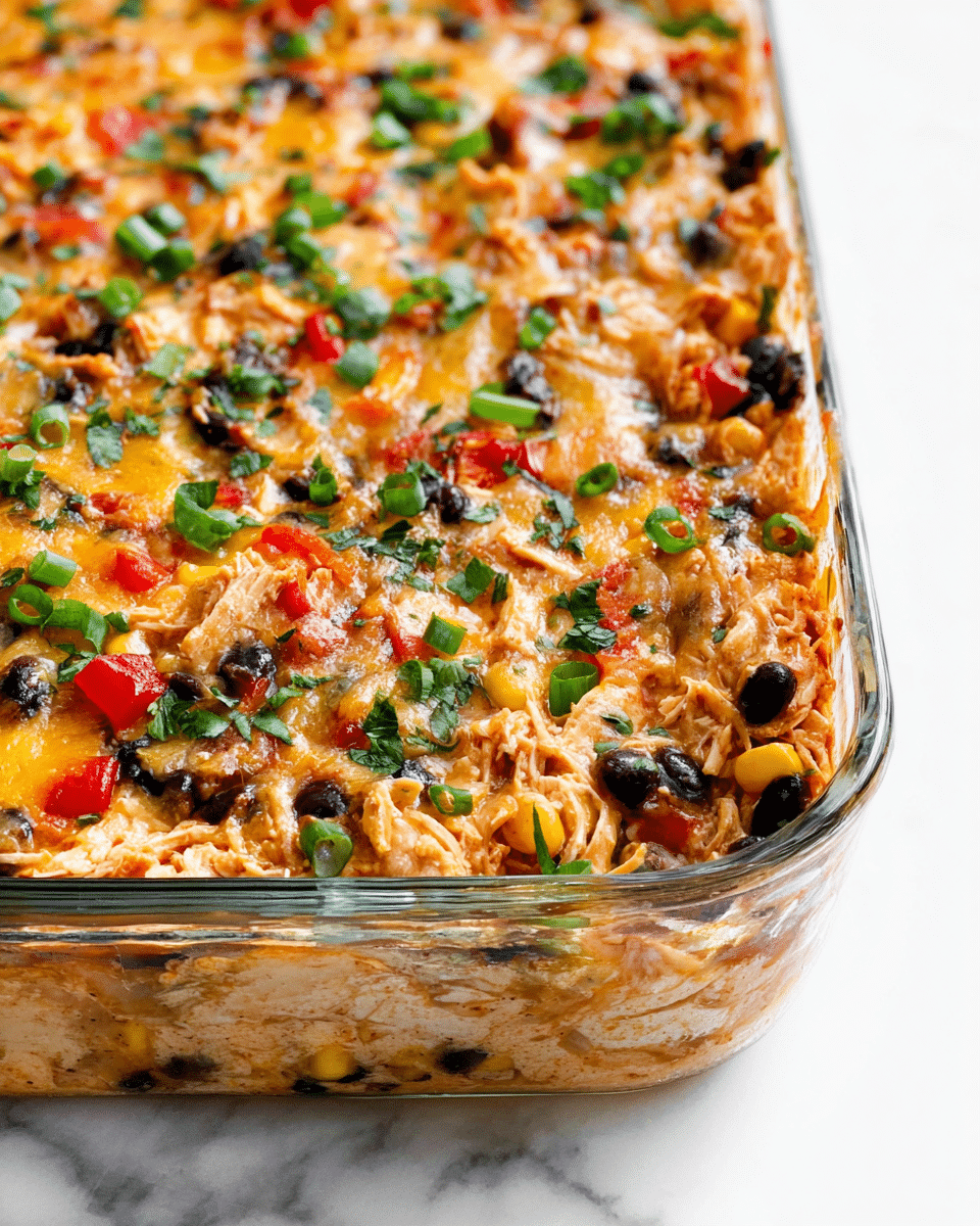 A close-up view of a baked casserole in a clear glass dish, showing a mix of shredded chicken, black beans, corn, small red bell pepper pieces, and melted cheese all combined evenly. The casserole surface is topped with scattered green herbs and sliced green onions, giving a fresh contrast to the warm orange, yellow, black, and light brown colors within the dish. The dish is placed on a white marbled surface, with the glass edges visible and some melted cheese sticking slightly to the sides. photo taken with an iphone --ar 4:5 --v 7
