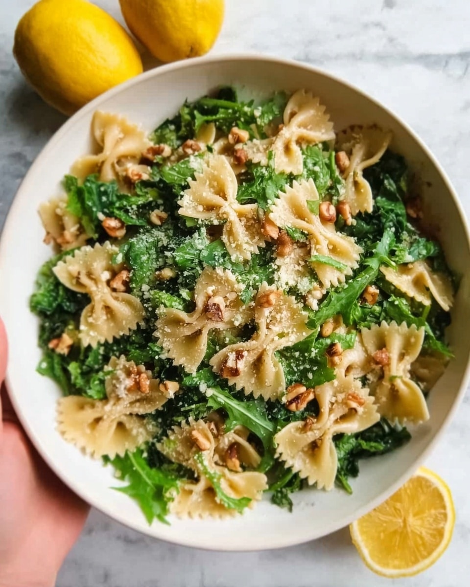 A white bowl filled with bowtie pasta mixed with green leafy kale and sprinkled with small pieces of nuts and grated cheese. The pasta is a light beige color with a smooth texture, while the kale adds a fresh, dark green color with a slightly rough texture. The nuts, golden brown and crunchy, are scattered evenly through the dish. The bowl sits on a white marbled surface with two lemons nearby, giving a fresh and natural feel. A woman's hand is reaching from the left side holding the bowl gently. Photo taken with an iphone --ar 4:5 --v 7