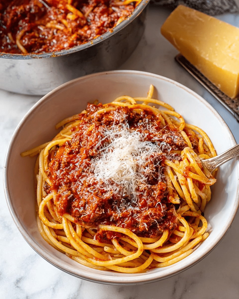 A white bowl filled with thick spaghetti noodles covered in a rich, chunky red meat sauce. On top, a generous layer of finely grated white cheese is sprinkled evenly, adding texture to the sauce. The bowl is placed on a white marbled surface, with a metal pot full of more of the same meat sauce partially visible in the background, and a piece of yellow cheese with a grater resting beside it. Photo taken with an iphone --ar 4:5 --v 7