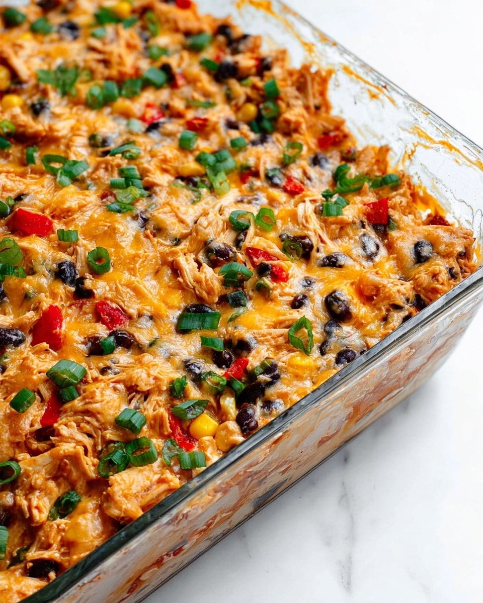 The image shows a clear glass baking dish filled with a colorful baked casserole made of shredded chicken, black beans, corn, chopped red peppers, and melted cheese. The dish has a mix of warm tones, like golden yellow from the corn and cheese, dark black from the beans, bright red from the peppers, and green from chopped herbs sprinkled on top. The casserole has a rough, uneven surface with visible small pieces of chicken and vegetables throughout, giving it a hearty, textured look. The dish is placed on a white marbled surface. photo taken with an iphone --ar 4:5 --v 7