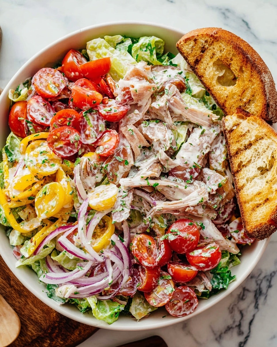 A large white bowl filled with a colorful salad made of several visible layers: the bottom layer is shredded green lettuce, followed by layers of thinly sliced purple onion, halved red cherry tomatoes, strips of light pink deli meat, pale yellow cheese slices, and bright yellow banana pepper slices, all mixed together and coated in a creamy white dressing speckled with pepper and herbs. Two golden brown toasted bread slices rest stacked on the right edge of the bowl. The bowl is placed on a white marbled surface with some whole cherry tomatoes on a white cutting board in the background. Photo taken with an iphone --ar 4:5 --v 7