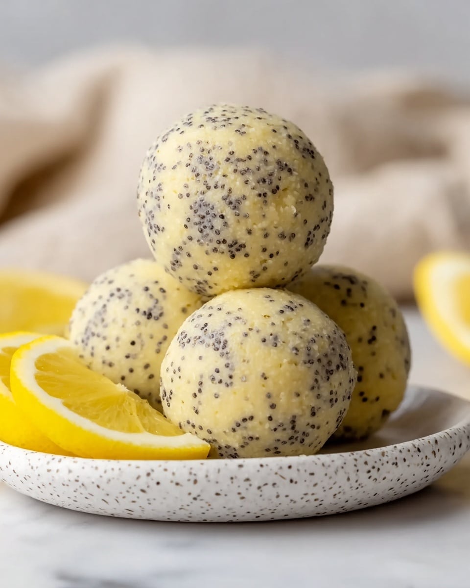 The image shows a close-up of four round balls covered with small black poppy seeds, giving them a speckled texture. The balls are pale yellowish in color and arranged closely together in a slightly stacked way on a white speckled plate. Around these balls, there are several fresh lemon slices with bright yellow peel and juicy, shiny light yellow flesh. The background is blurred with soft, light fabric folds, and the surface beneath the plate is a white marbled texture. photo taken with an iphone --ar 4:5 --v 7