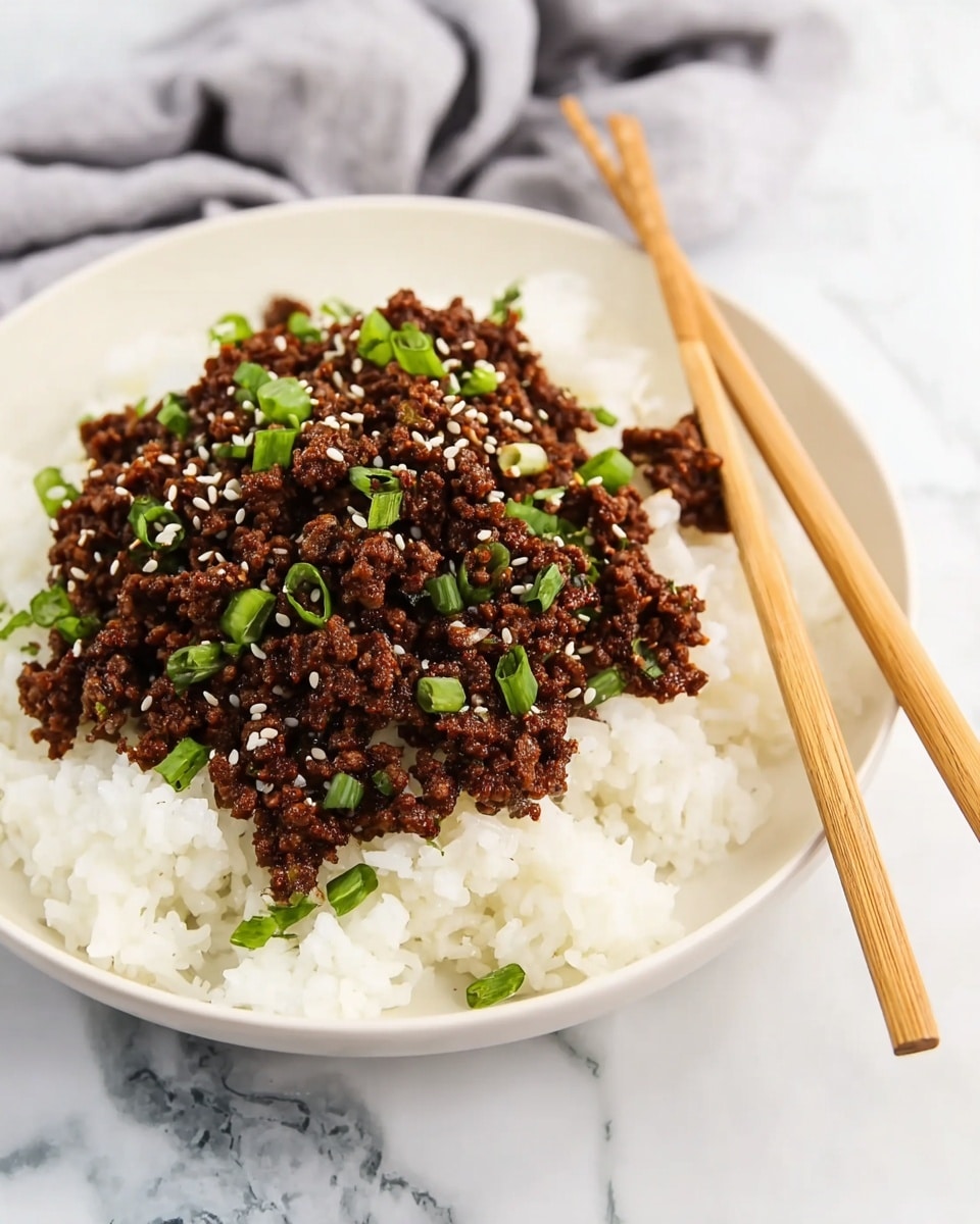 A white bowl contains two main layers: a base layer of soft, fluffy white rice covering the bottom, and on top, a generous layer of cooked, finely crumbled ground meat with a rich brown color. The meat is sprinkled with small, white sesame seeds and chopped green onions, adding bright green accents. A light-colored pair of chopsticks rests on the rim of the bowl. The bowl is placed on a white marbled surface with a gray cloth softly blurred in the background. Photo taken with an iphone --ar 4:5 --v 7